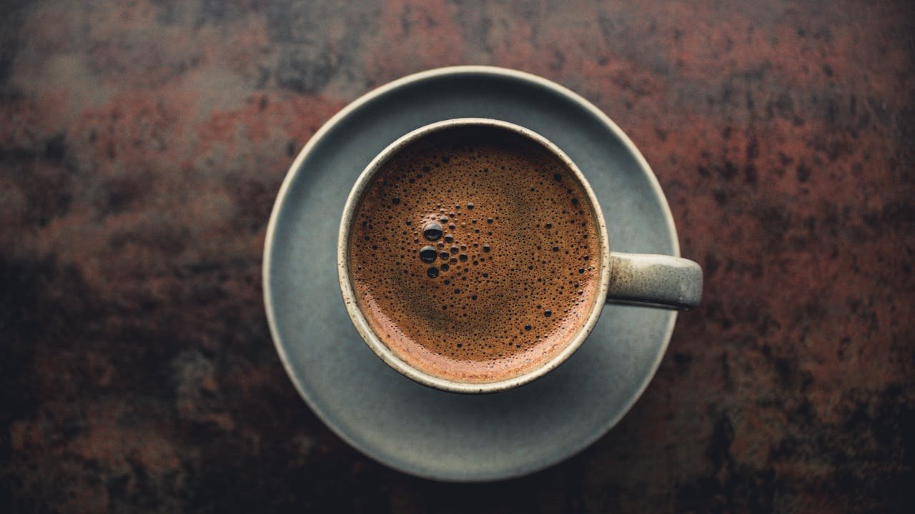 Top view of a hot espresso in a rustic ceramic mug on a dark textured surface.