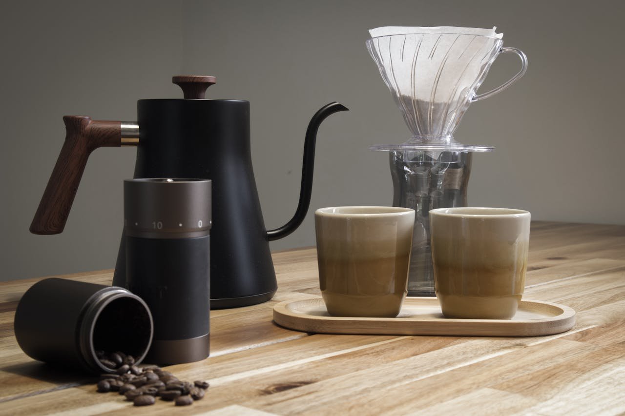 A stylish selection of coffee brewing tools including a V60 dripper, kettle, and grinder on a wooden table.