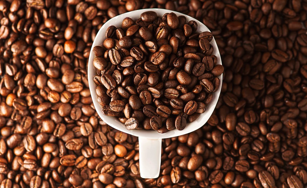 Close-up photo of roasted coffee beans in a mug surrounded by more beans. Ideal for coffee lovers.